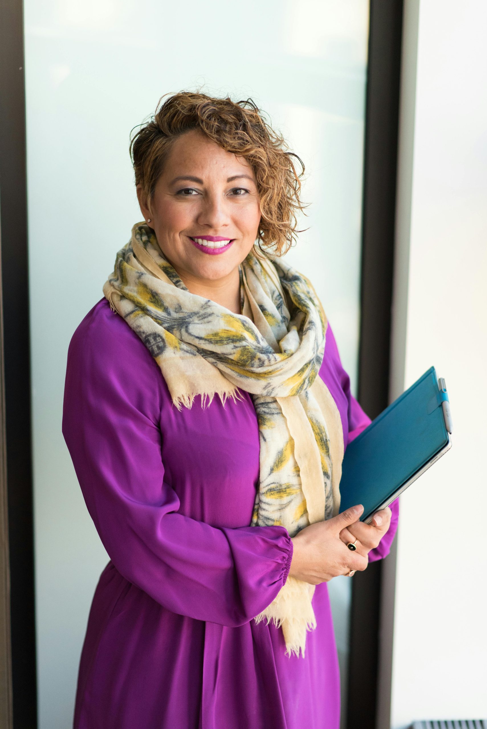 pexels-photo-1181424-1181424 Smiling woman in a purple dress and scarf holding a tablet indoors.