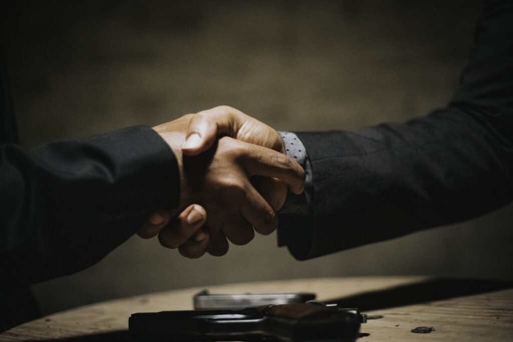 Two people shaking hands across a table after agreeing a business sale
