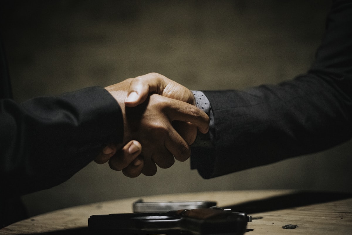 Two people shaking hands across a table after agreeing a business sale