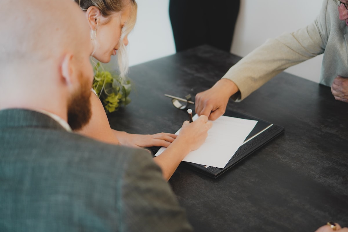 Reading the whole offer Two people reviewing and signing deal documents at a desk