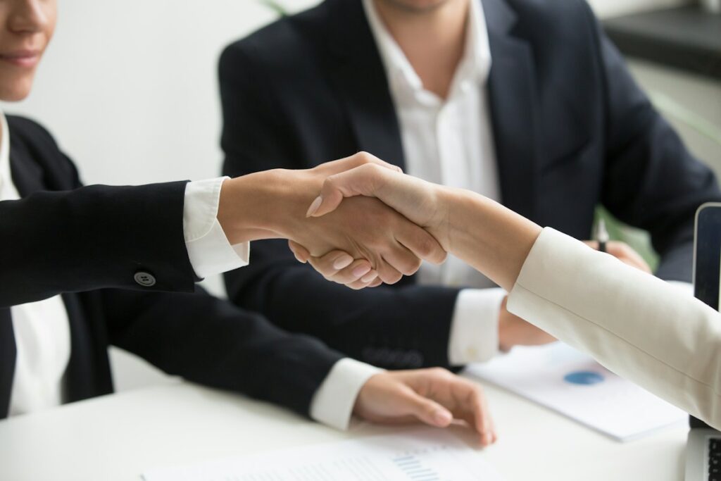 Two professionals shaking hands across a desk after an agreement
