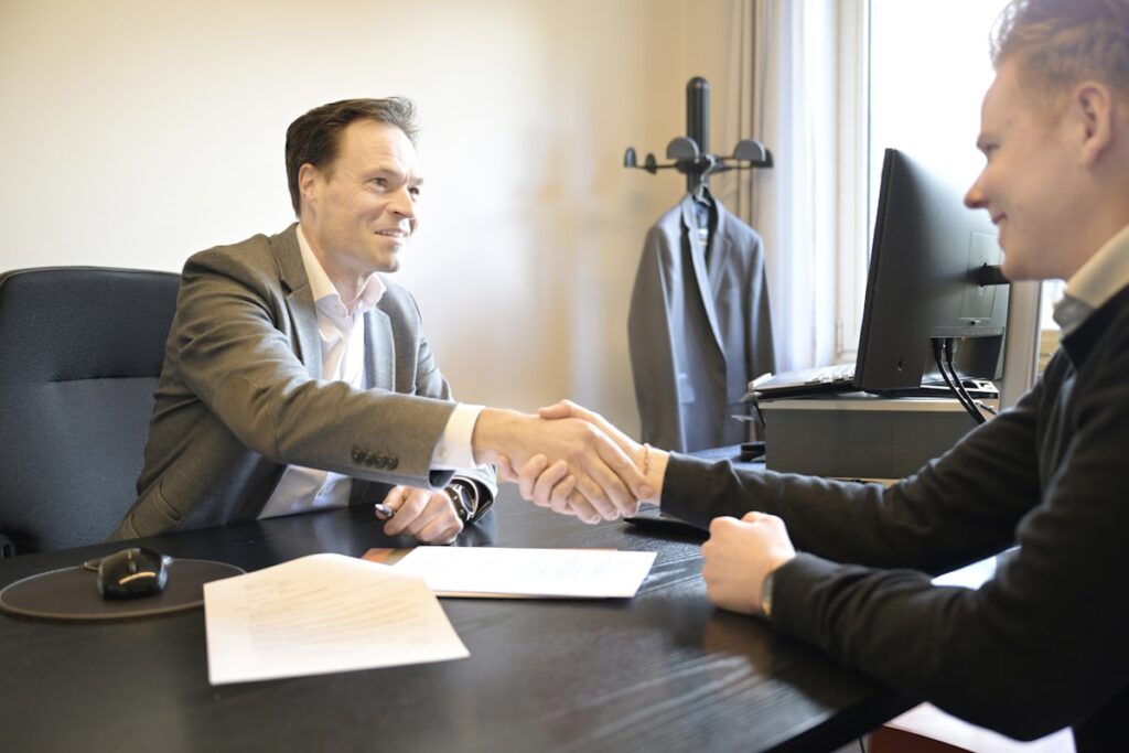 Business advisor and client shaking hands across an office desk after agreeing acquisition terms